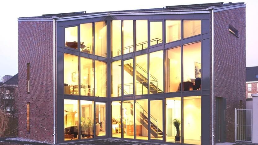 Moderne, mehrstöckige Wohnung mit großflächigen Fenstern und Treppe, beleuchtet bei Dämmerung.