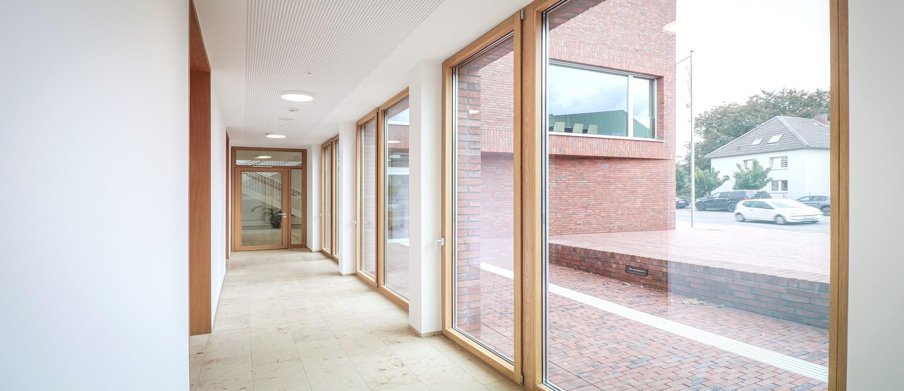 Heller Flur mit großen Fenstern und Sicht auf einen Innenhof, umgeben von roten Backsteinwänden.