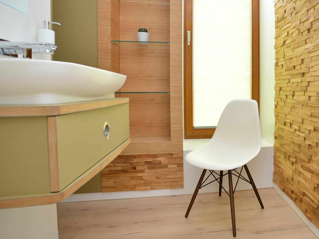 Helles Badezimmer mit Holzregal, modernem Waschbecken und weißem Stuhl neben einem Fenster mit Jalousien.