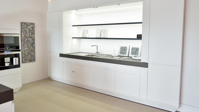 Moderne weiße Küche mit schwarzer Arbeitsfläche, Spüle und offenen Regalen, vor neutralem Hintergrund.