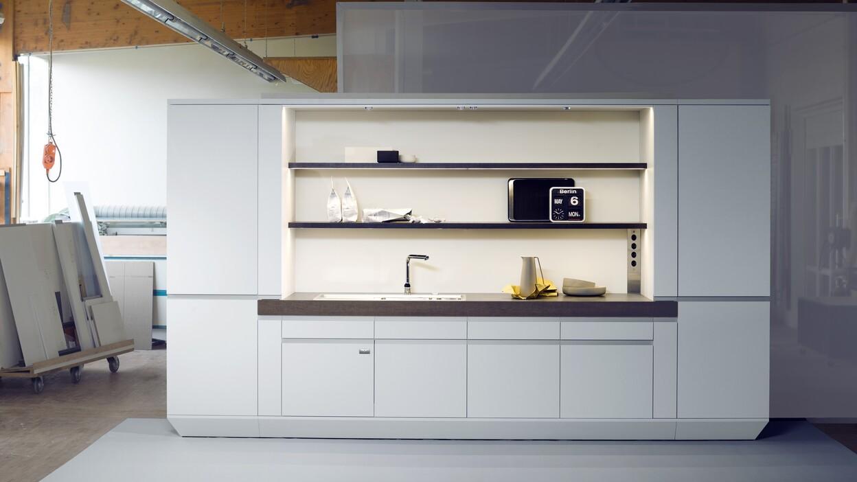 Moderne, weiße Küchenzeile mit Spüle, Regalen und Elektrogeräten in einem Werkstattumfeld.