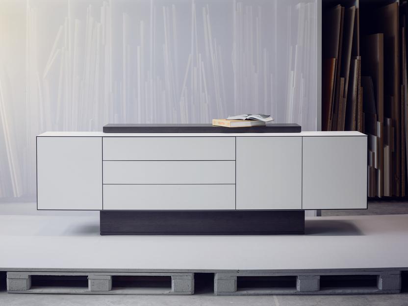 Minimalistisches Sideboard mit Schubladen und offenen Fächern, auf einer Palette in einem modernen Raum.