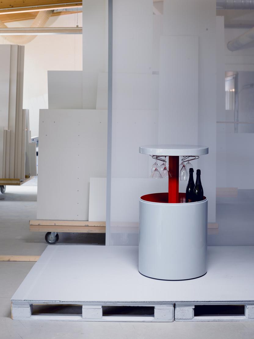 Weißer Getränkewagen mit roten Akzenten, umgeben von weißen Paneelen und einem klaren Raum, im Hintergrund ausgestellte Materialien.