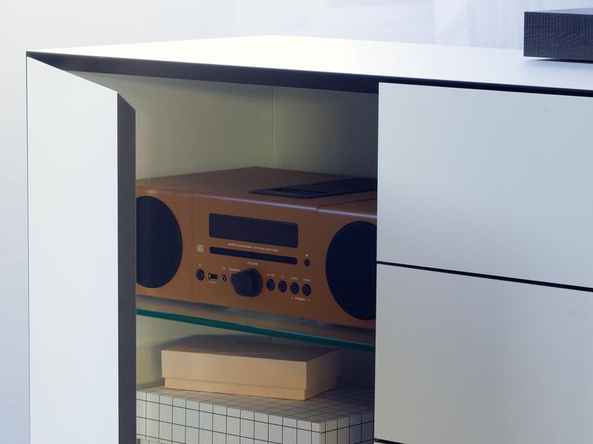 Offene Schublade eines Möbelstücks mit einem Radio und mehreren Kisten in neutralen Farben.