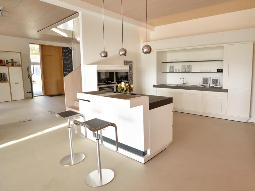 Moderne, helle Küche mit Kochinsel, integrierten Geräten und Barhockern in minimalistischem Design.