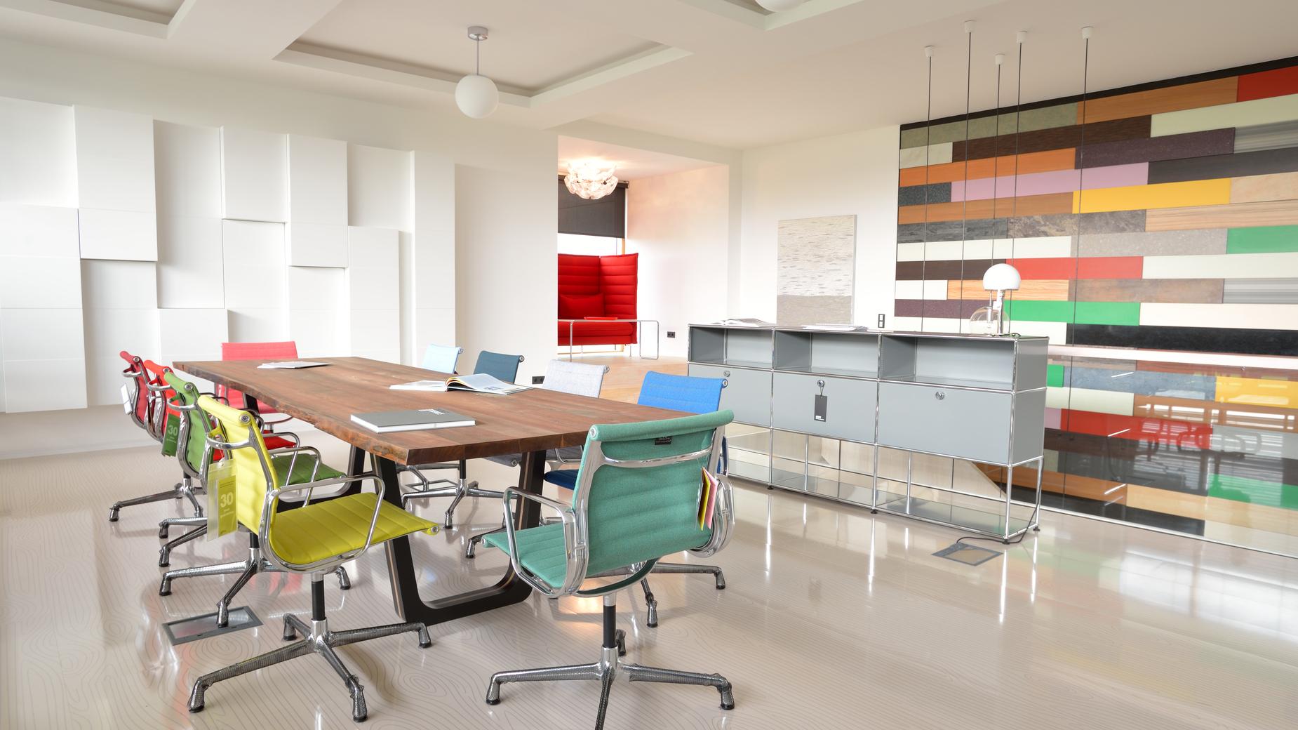 Modernes Büro mit langem Holztisch, bunten Stühlen und einer farbigen Wandgestaltung im Hintergrund.