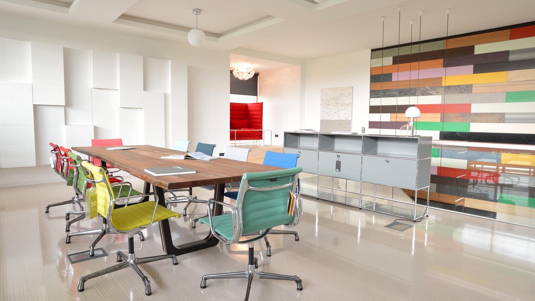 Modernes Büro mit langem Holztisch, bunten Stühlen und einer farbigen Wandgestaltung im Hintergrund.