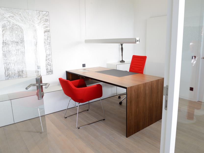 Modernes Büro mit Holzschreibtisch, zwei roten Stühlen und einer großen Lampe, hell und minimalistischen Möbeln.