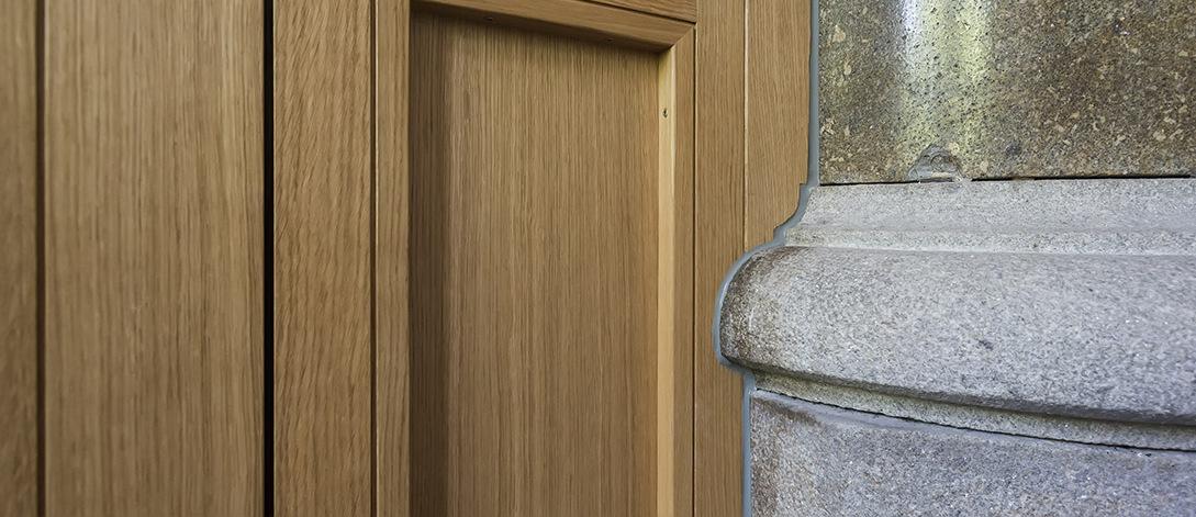 Detailaufnahme einer Holzverkleidung neben einem grauen Säulenschaft aus Stein.